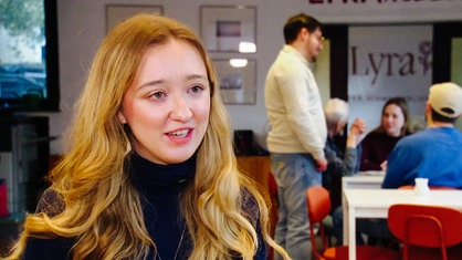 Portrait einer jungen Frau mit langen, blonden Haaren. Im Hintergrund sieht man Besucher im Union Salon.