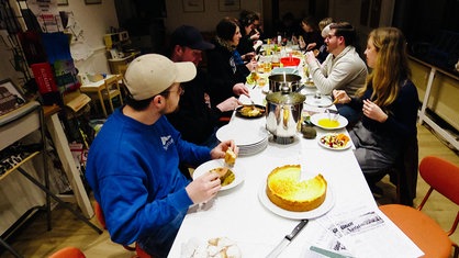 Menschen sitzen gemeinsam an einer Tafel und essen. 