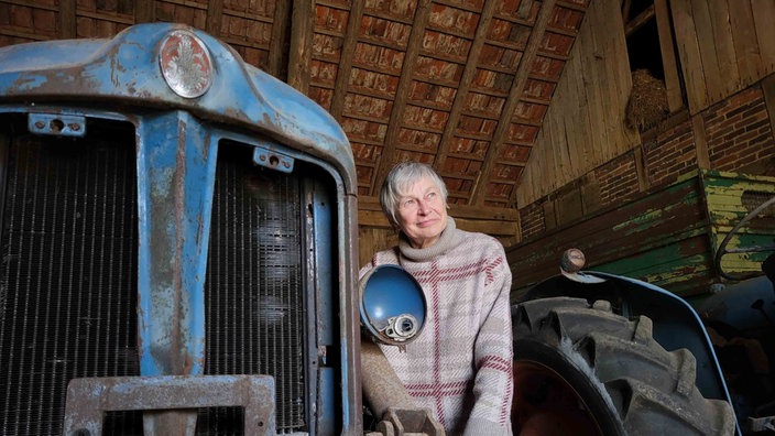 Marianne Lütkehölter steht in ihrer Scheune in Bielefeld neben einem alten blauen Traktor.