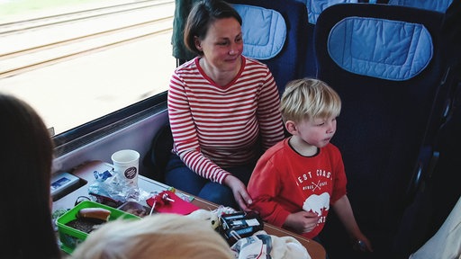 Eine Frau im geringeltem T-Shirt sitzt mit einem kleinen Jungen in einem Zugsitz. 