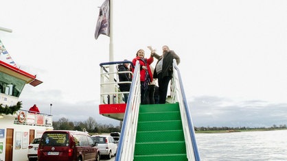 Frau und Mann stehen auf einer Treppe der Rheinfähre. Sie winken.