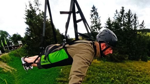 Ein Mann fliegt in einer Halterung über Bäume hinweg.
