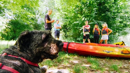 Familie Wick, Dominik Kopitzke und Hund Ares stehen am Ufer der Erft. Sie stehen vor einem gelb-roten Kajak.
