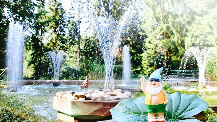 Ein Springbrunnen. Zwischen den kleinen Wasserfontänen stehen Gartenzwerge.