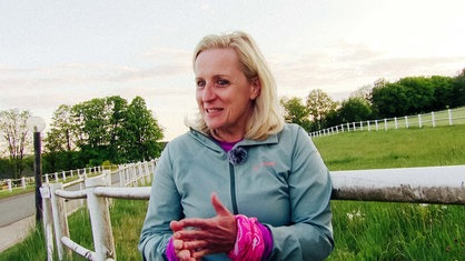 Sandra Wiedemann steht vor einer Wiese. Sie schaut in die Ferne.