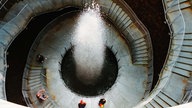 Während der Landesgartenschau Bad Oeynhausen im Jahr 2000 stehen mehrere Menschen  in einer Art Treppenhaus um einen Wasserkrater herum.