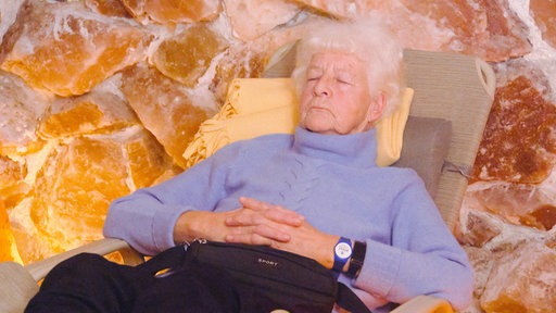 Eine Seniorin sitzt mit geschlossenen Augen in einem Liegestuhl in der Salzgrotte.