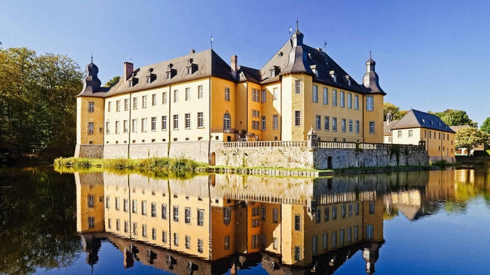 Ein gelbes Schloss. Es ist umgeben von Wasser.