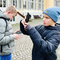 Zwei Jungs stehen mit einem Handy und einem Tablet vor dem Schloss Morsbroich