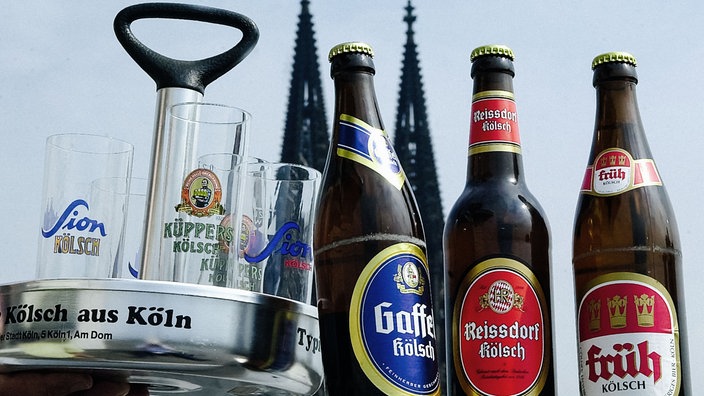 Ein Tablett steht neben mehreren Flaschen Kölsch, im Hintergrund ist der Kölner Dom.