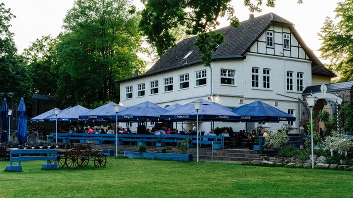 Ein großes weißes Haus. Davor ein Biergarten.