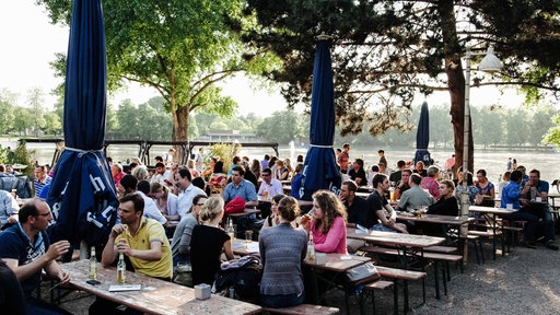 Menschen sitzen in einem Biergarten am Rhein.