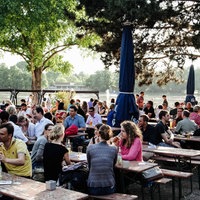 Menschen sitzen in einem Biergarten am Rhein.