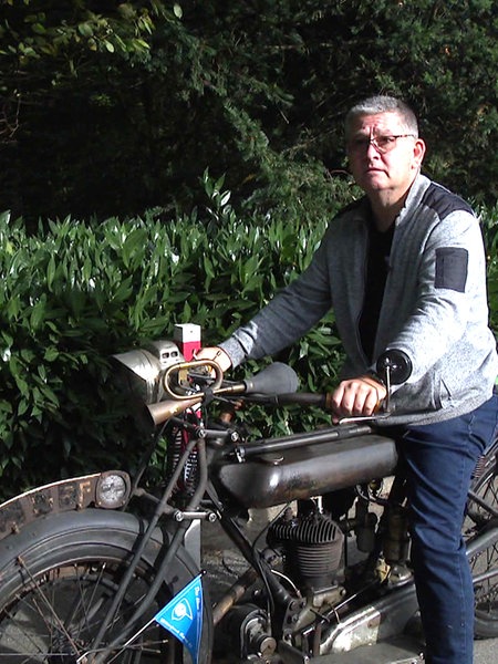 Stephan Homberger sitzt auf einem 100 Jahre alten Motorrad der Marke NSU