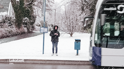 Ein Junge steht im Schnee an einer Bushaltestelle und beobachtet einen vorbeifahrenden Bus