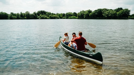 Eine dreiköpfige Familie mit einer kleinen Tochter fährt im Kanu auf den See hinaus.