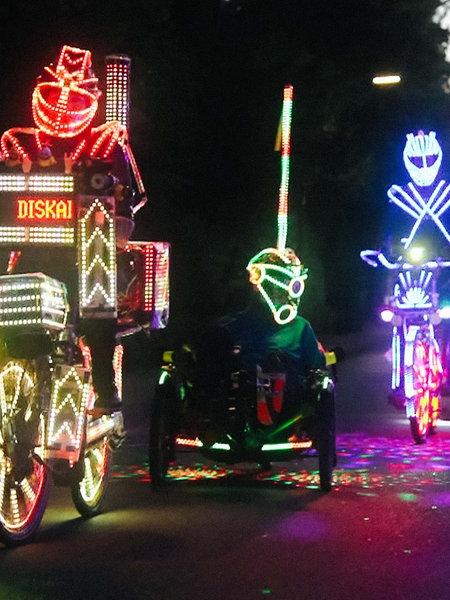 Fünf Personen fahren neben- und hintereinander Fahrrad. Sie sind mit LED-Lichtern geschmückt.