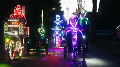 Fünf Personen fahren neben- und hintereinander Fahrrad. Sie sind mit LED-Lichtern geschmückt.