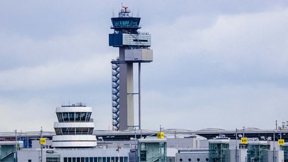 Auf einem Flughafengelände stehen zwei Flugzeuge und im Hintergrund ist der Tower zu sehen.