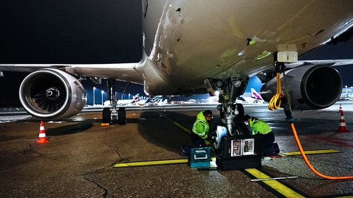 Fluggerätmechaniker Adam kniet vor einem Flugzeugreifen und tauscht ihn mit einem Kollegen aus
