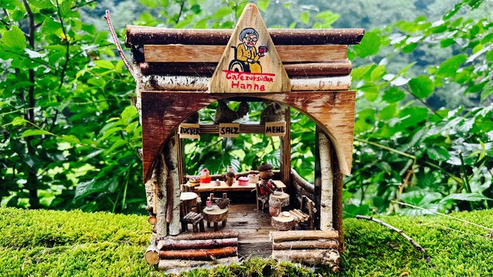 Ein kleines Haus aus Ästen stellt ein kleines Wichtelcafé dar. Es gibt Miniatur Stühle und Tische.