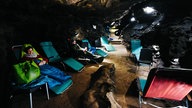 Zwei Menschen sitzen auf Liegestühlen, die an einem Gang in der Kluterthöhle stehen.