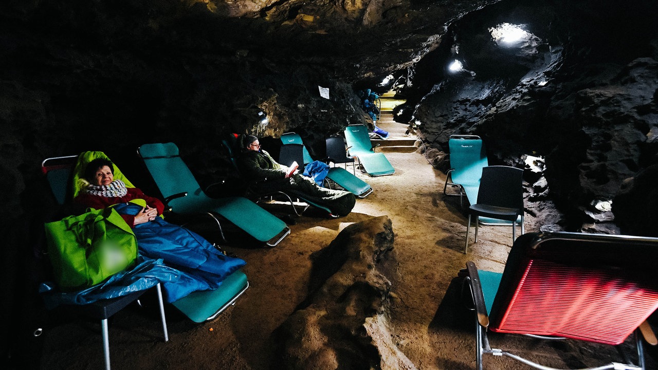 Zwei Menschen sitzen auf Liegestühlen, die an einem Gang in der Kluterthöhle stehen.
