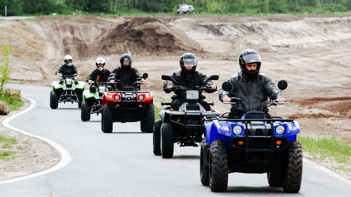 Fünf Männer sitzen auf Quads und fahren über eine Straße.