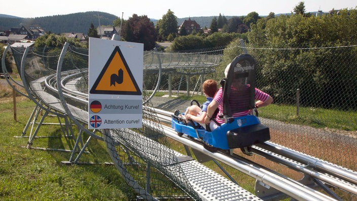 Eine Frau und ein Kind fahren auf der Sommerrodelbahn in Winterberg.