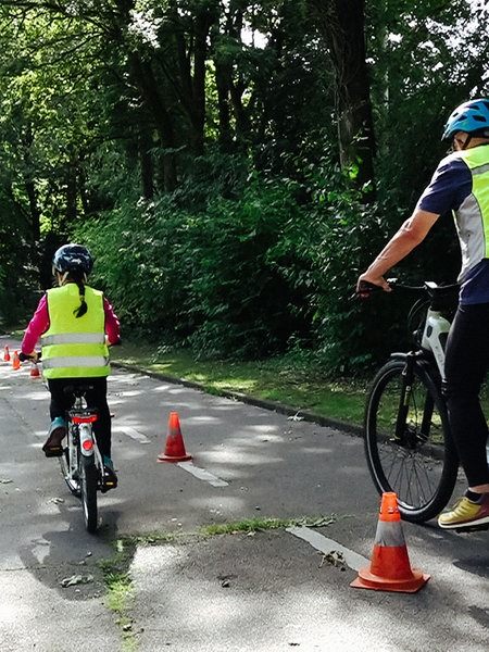 Ein Kind und ein Erwachsener fahren mit ihren Fahrrädern nebeneinander eine mit Pylonen abgesteckte Strecke.