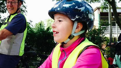 Opa Jürgen Brauweiler und Enkelin Luna fahren einen Fahrradparcours mit Helm und Warnweste.