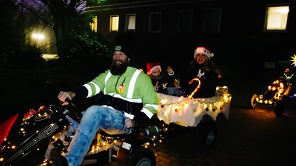 Eine Familie fährt in hell geschmücktem Go-Kart mit Anhänger voller Lichterketten bei der Fünkchen-Fahrt mit.
