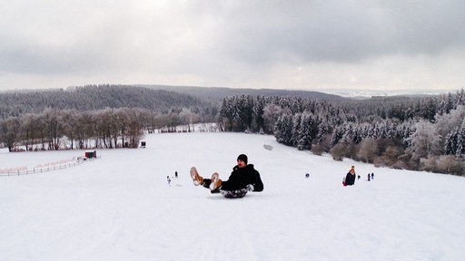 Ein Mann rodelt den Hang im Wintersportgebiet Weißer Stein bei Hellenthal hinunter.