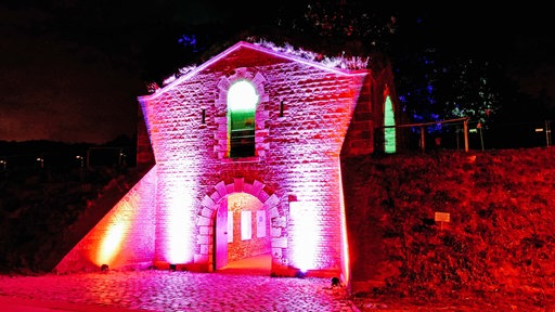 Ein Torbogen. Er wird von pinken und roten Strahlern erleuchtet.