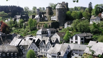 Auf einem kleinen Berg steht die Monschauer Burg. Rund um den Hügel stehen viele Fachwerkhäuser.