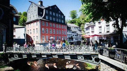 Im Vordergrund eine kleine Brücke. Im Hintergrund ein großes rotes Haus.