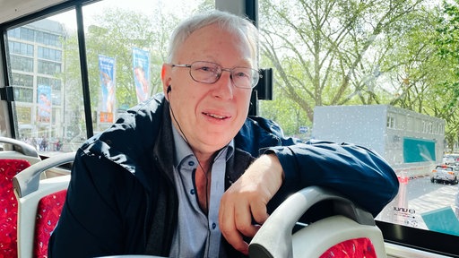 Hans Peter Detjen, ein älterer Mann mit weißem Haar, sitzt auf dem Oberdeck eines Doppeldeckerbusses und lächelt.