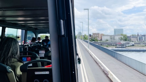 Touristen sitzen auf dem Oberdeck eines Hop-on-Hop-off-Busses bei einer Fahrt durch Düsseldorf.