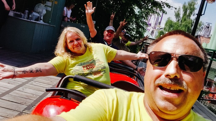 Jürgen Nießen sitzt mit anderen Mitgliedern des "Freundeskreises Kirmes und Freizeitparks" in einer Achterbahn.