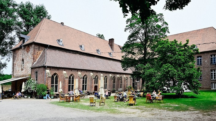 Das ehemalige Kloster Graefenthal in Goch von außen. An mehreren Tischen davor sitzen Menschen.