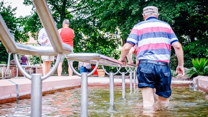 Mehrere Menschen halten sich am Geländer eines Kneipp-Beckens fest und gehen durchs Wasser.