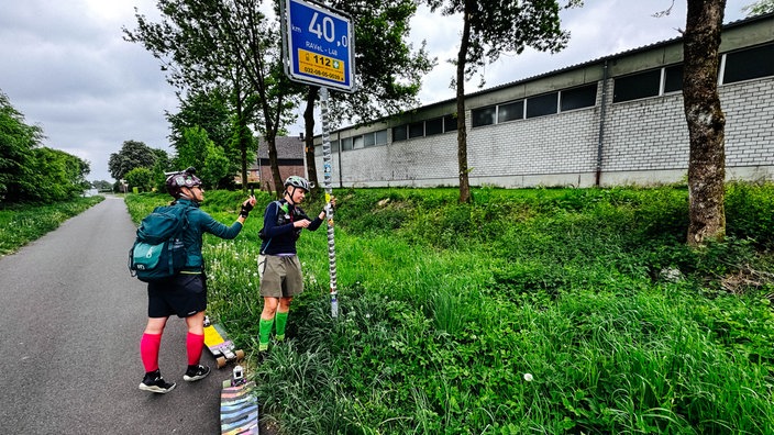 Die Ultra-Longboarderinnen Lena Meringdal und Viola Weinert kleben auf einen Schilderpfosten einen "Wir waren hier"-Sticker