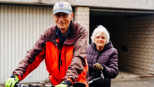 Ein älteres Paar sitzt gemeinsam auf einem Tandem. 