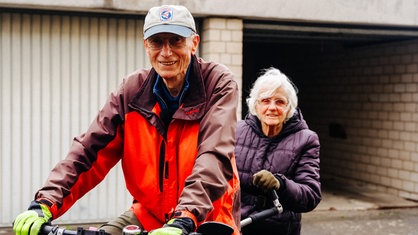 Ein älteres Paar sitzt gemeinsam auf einem Tandem. 