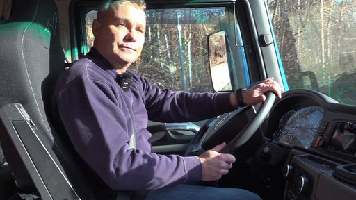 Alexander Herpich mit blauem Pullover, sitz auf dem Fahrersitz eines Lkws und hält das Lenkrad mit beiden Händen fest