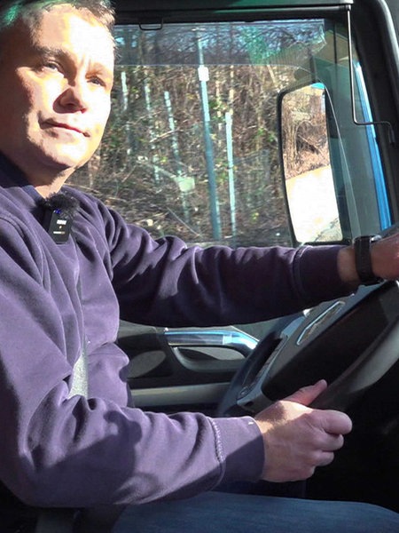 Alexander Herpich mit blauem Pullover, sitz auf dem Fahrersitz eines Lkws und hält das Lenkrad mit beiden Händen fest