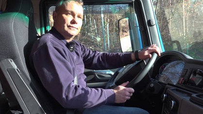 Alexander Herpich mit blauem Pullover, sitz auf dem Fahrersitz eines Lkws und hält das Lenkrad mit beiden Händen fest