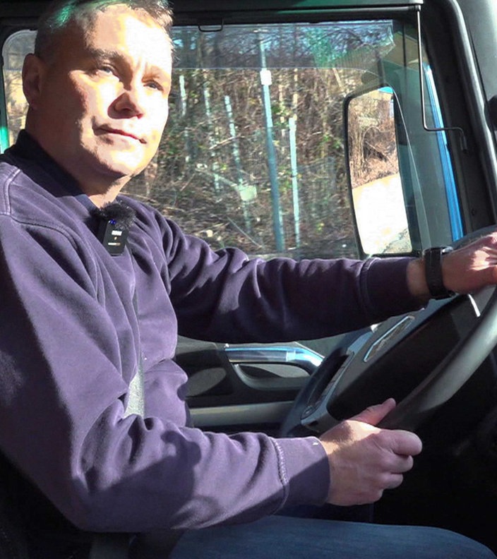Alexander Herpich mit blauem Pullover, sitz auf dem Fahrersitz eines Lkws und hält das Lenkrad mit beiden Händen fest