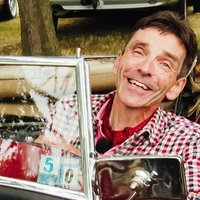 Markus Grünhagen sitzt in einem rot-blau karierten Hemd in einem roten Oldtimer und lächelt.