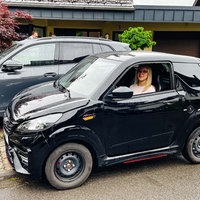 Johanna König sitzt in ihrem Mopedauto, das deutlich kleiner ist, als das dahinter geparkte, normale Auto.